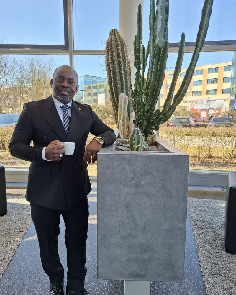 Romial Kenmogne im dunklen Anzug mit einer Tasse Kaffee